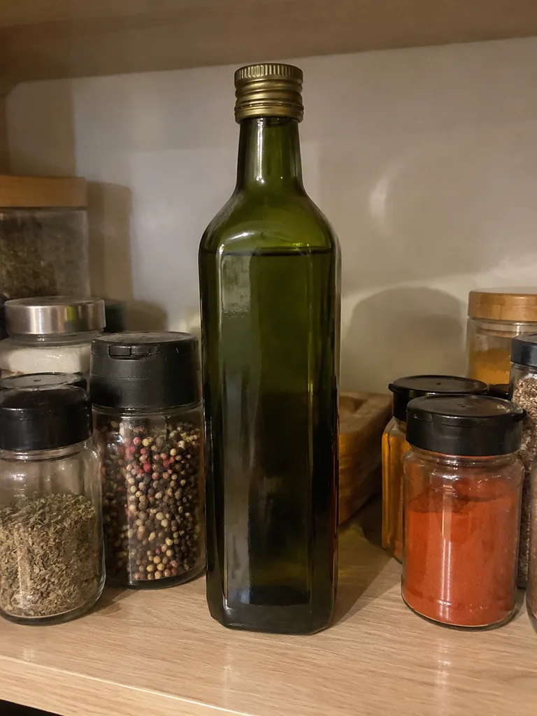 Тёмно-зелёная бутылка масла на кухонной полке среди специй